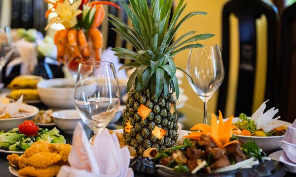 Close up of a table with some food, a big pineapple and two wine glasses.