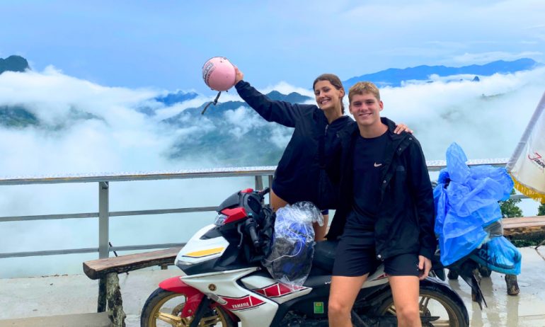 A couple on a motorbike with Ha Giang view in clouds behind.