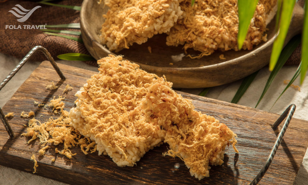 A wooden cutting board with a big piece of Ninh Binh burnt rice and pork floss.