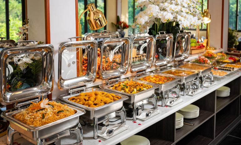 A table with six trays of buffet food.