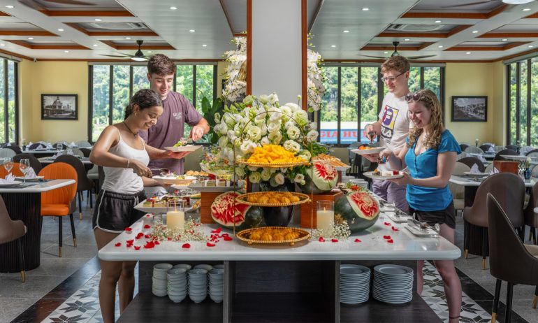 Four guests taking food at the buffet station of cozy restaurant.