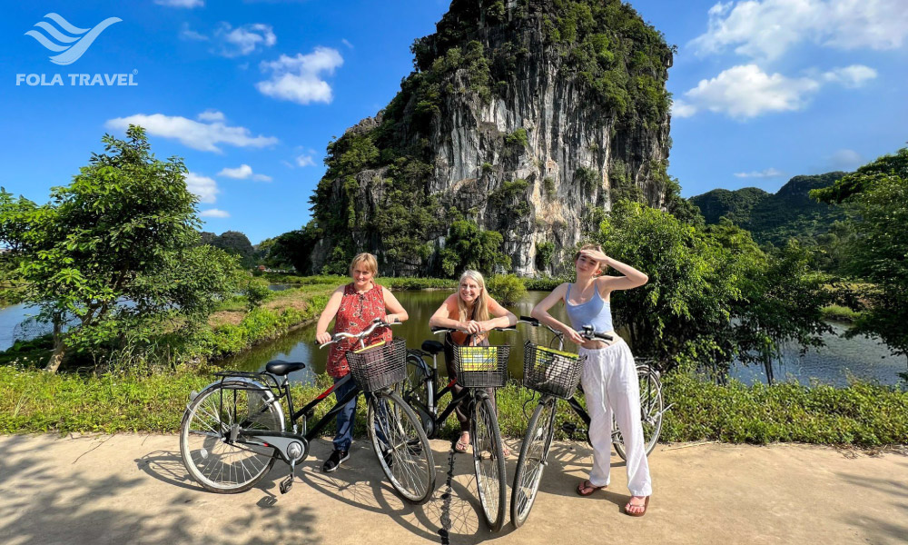 Three girls stop on a road with three bikes in front of a large limestone mountain.