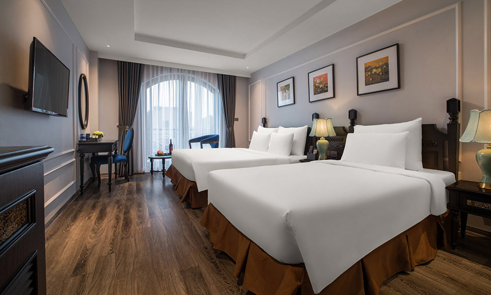 A room with two white beds facing the TV and a make up counter.