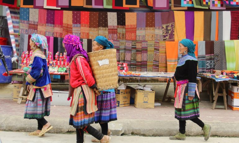 Ethnic women walking pass a textile stall.