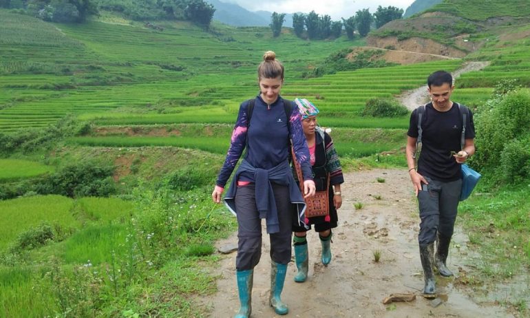 Two people trekking with an ethnic woman among the rice field.