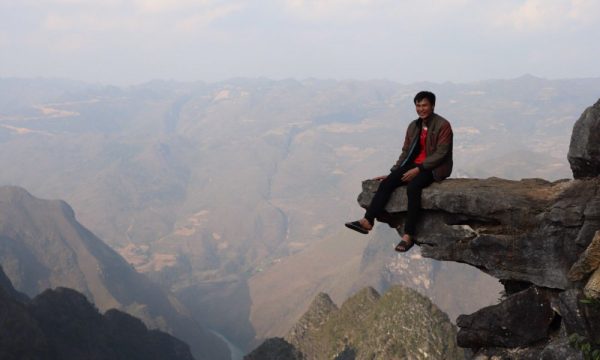 A man sitting on a rock with view behind.