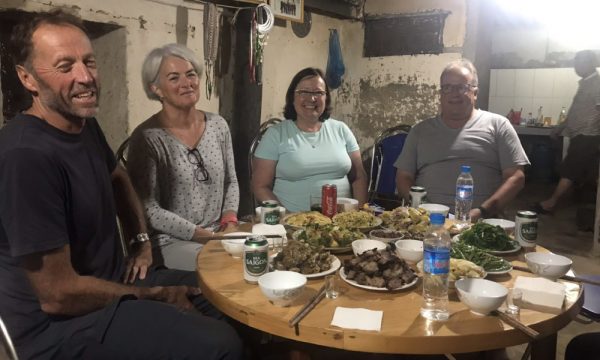 Four people sitting on a table with Vietnamese food in front of them.