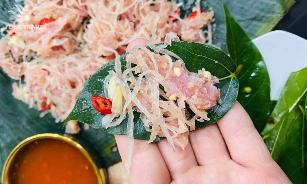 A hand holding a leaf with some nem chua on it, and a spicy sauce on the left.