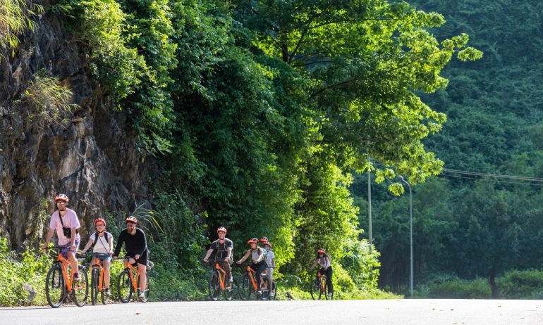 Ninh Binh guests cycling on the road with view of forests and mountains.