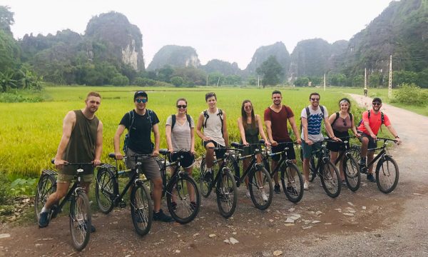 A row of Ninh Binh tourists on their bikes, in front of a rive field and mountains.