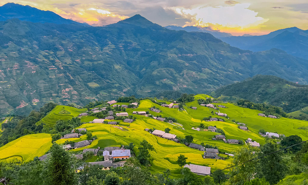 Ha Giang rice terraces on the bottom with many houses, looking out to the mountains.