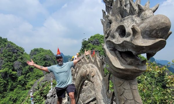 A man spead his arms next to the Hang Mua stone dragon.