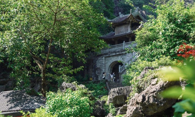 A few guests standing in front of a pagoda inside Trang An, surrounded by forests.