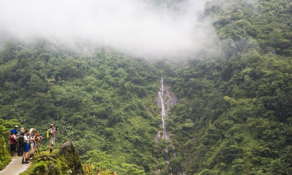 Tourists on the left taking photo of a waterfall.