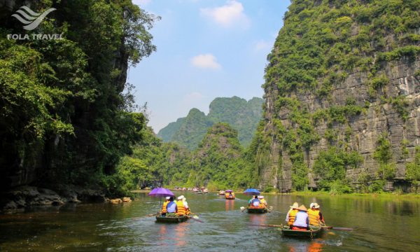 People on boats riding on a river through some limestone mountains.