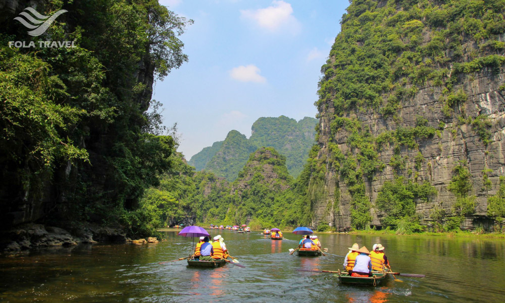 People on boats riding on a river through some limestone mountains.