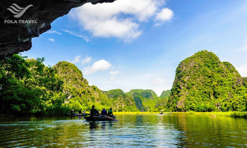 A boat going through a cave with an open space of water and mountains.