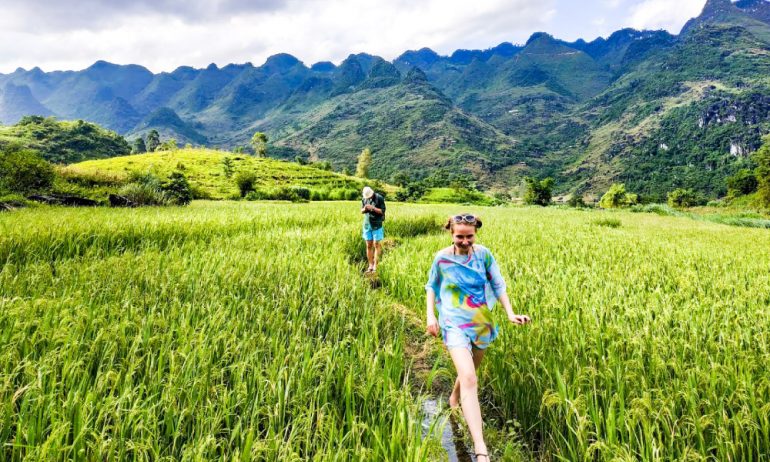 Two tourists walking in the middle of green fields.