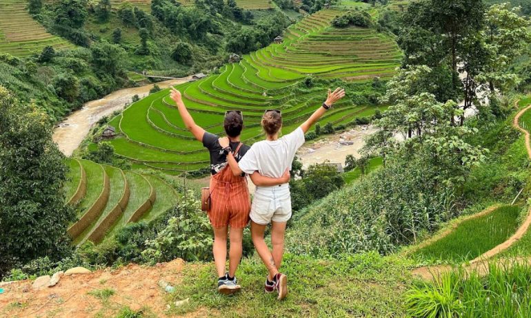 Two women in front of Sapa rice fields and stream scenery.