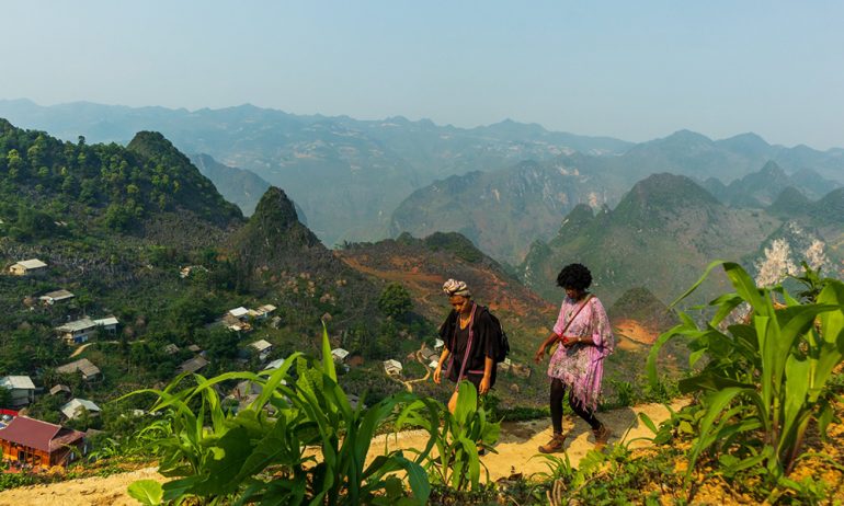 Two women trekking with Ha Giang mountains behind.